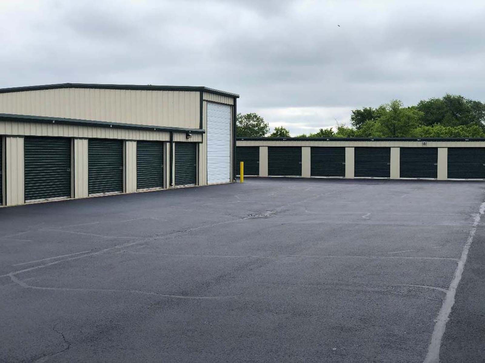 Empty asphalt lot beside beige storage units under a cloudy sky