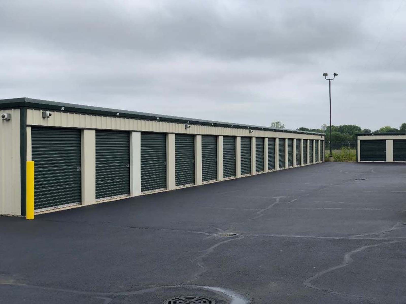 Row of storage unit doors under a cloudy sky beside an empty asphalt lot