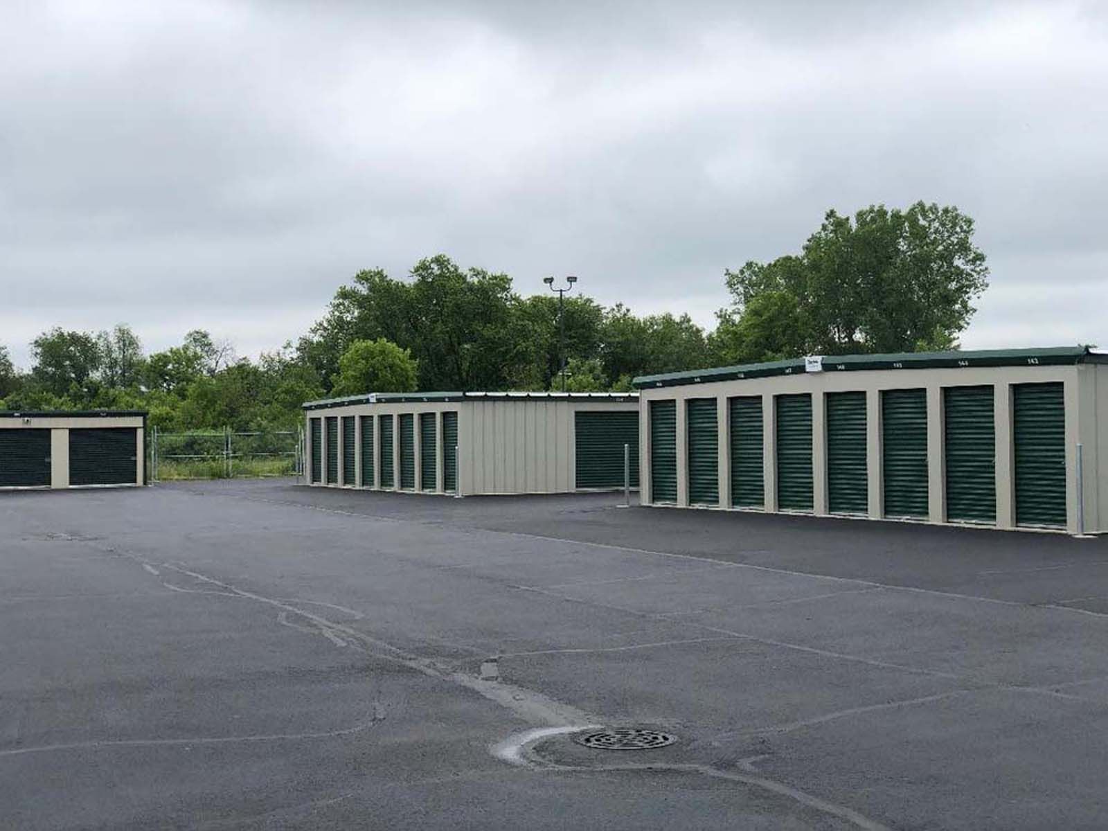 Row of green and beige storage units on a paved lot under an overcast sky