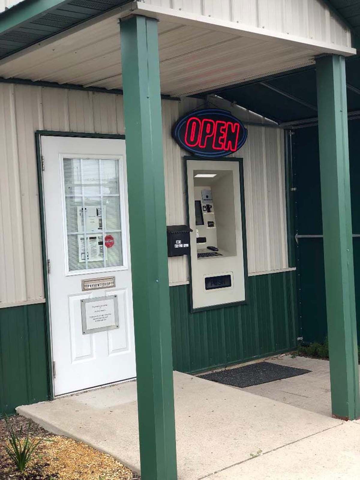 Storefront entrance with a neon “OPEN” sign and a white door under a covered porch.