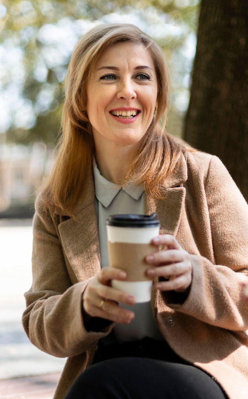A woman wearing a floral shirt and jeans is smiling.