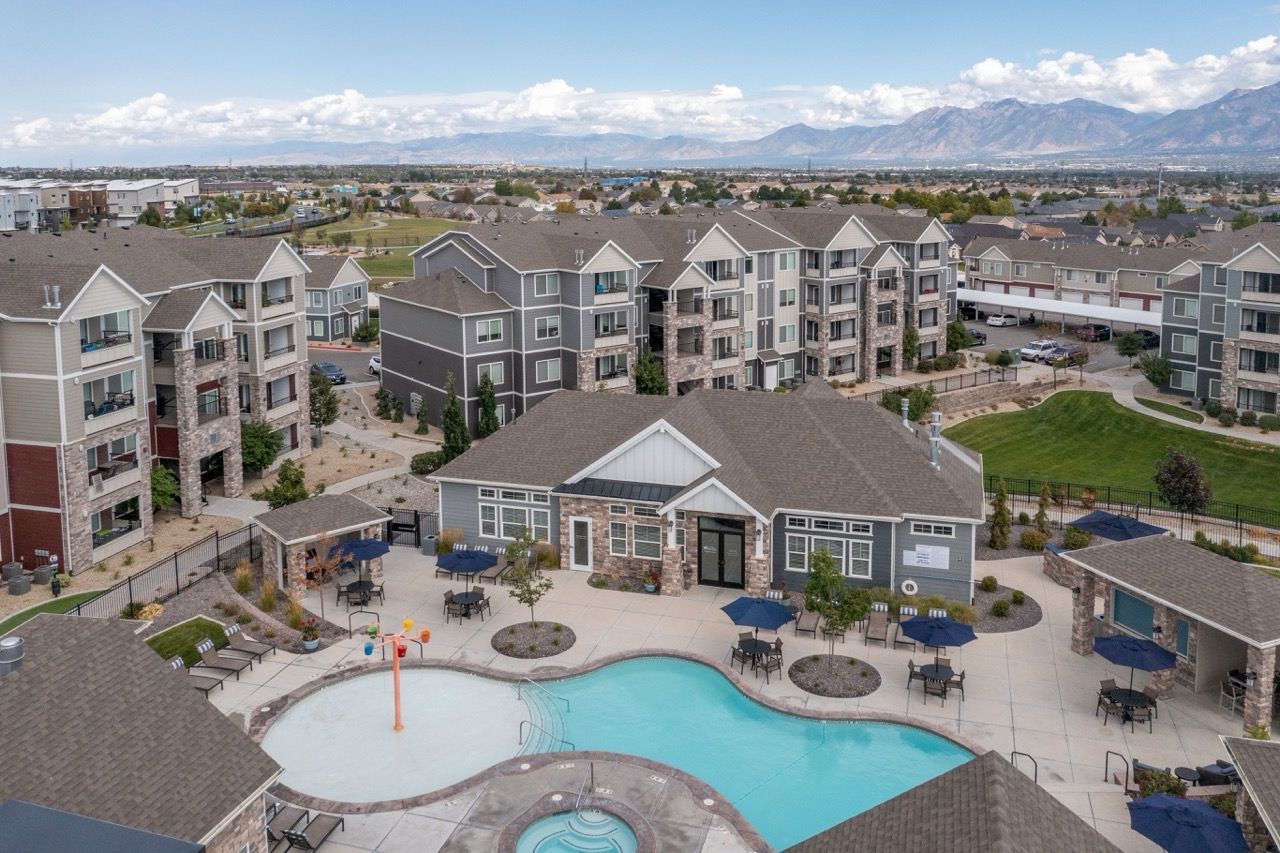 Aerial view of a modern apartment community with a central pool, clubhouse, and surrounding buildings at Herriman Towne Center in Herriman, UT.