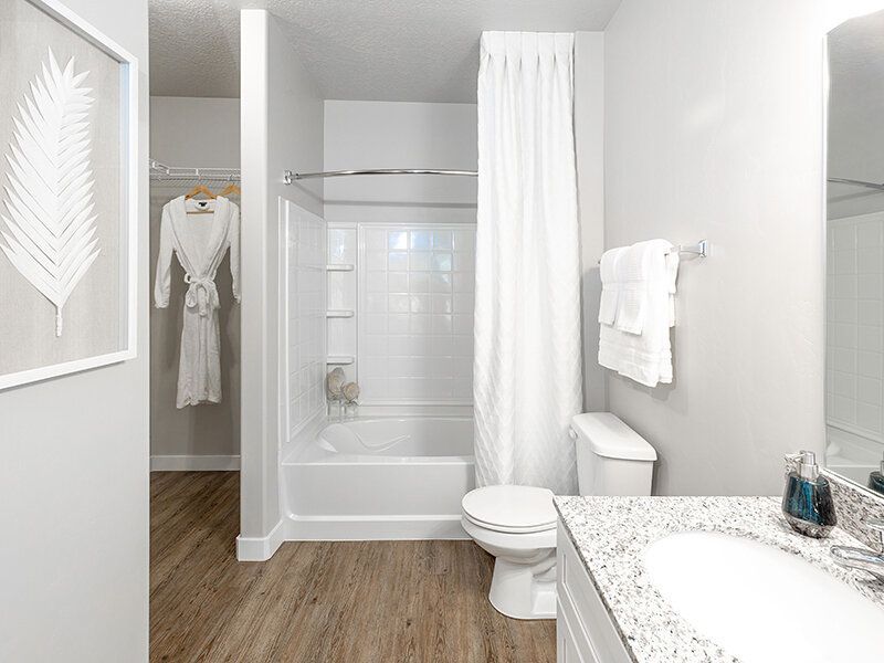 Bright apartment bathroom with a white tub/shower, toilet, and granite vanity at Herriman Towne Center in Herriman, UT.