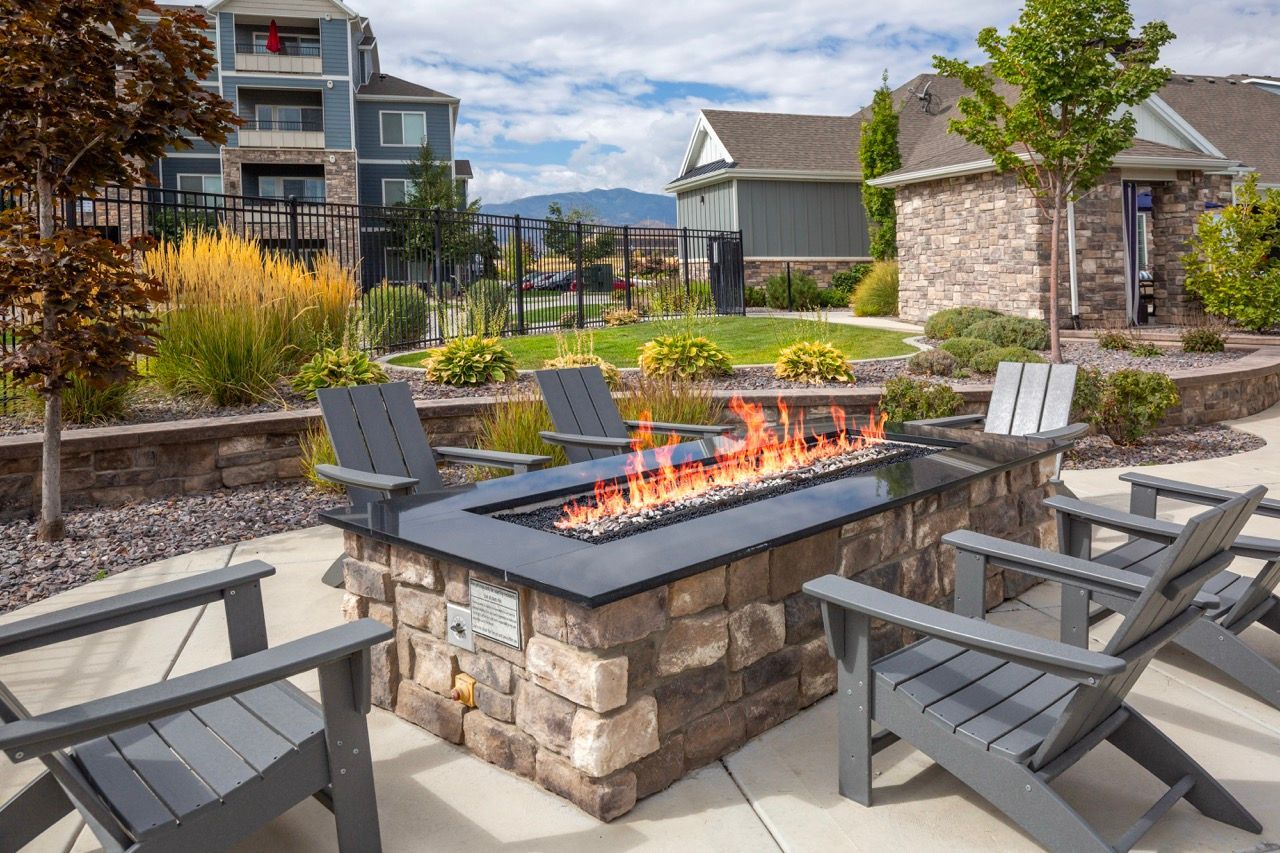 Outdoor communal fire pit with a stone surround and surrounding chairs in a landscaped courtyard at Herriman Towne Center in Herriman, UT.