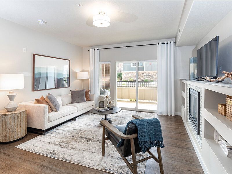 Bright apartment living room with sofa, chair, and balcony access at Herriman Towne Center in Herriman, UT.