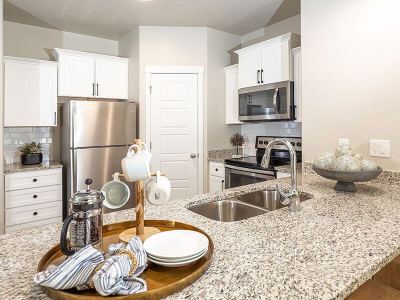 Modern white kitchen with granite countertops and stainless steel appliances at Herriman Towne Center in Herriman, UT.