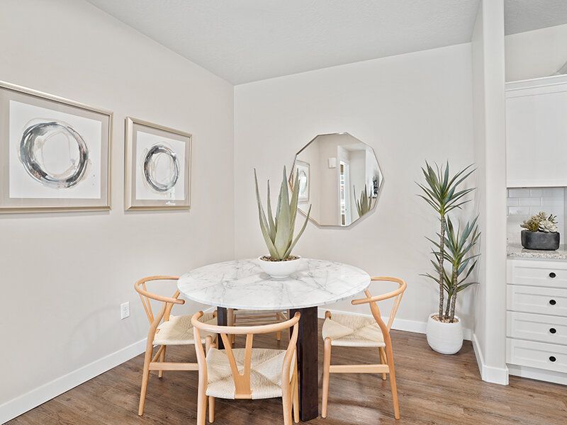 Interior dining area with round marble table, four wooden chairs, plants, and kitchen in the background at Herriman Towne Center in Herriman, UT.