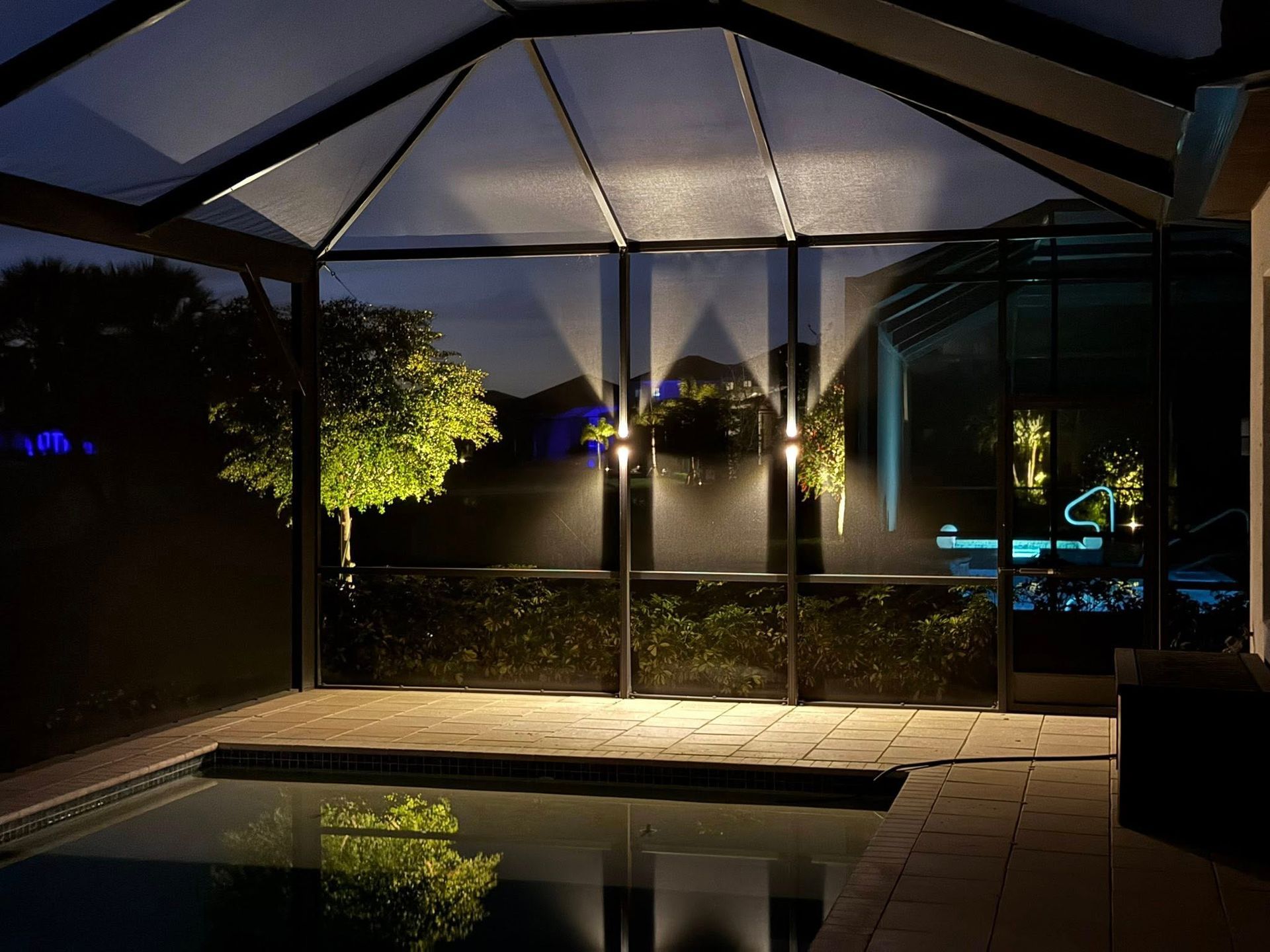 Covered outdoor pool at night with warm lights reflecting on the water and surrounding patio.
