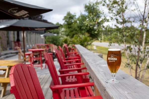 A glass of beer is sitting on a wooden deck next to a row of red chairs.