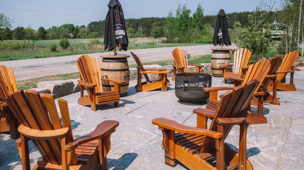 A row of wooden chairs are sitting on a patio next to a fire pit.