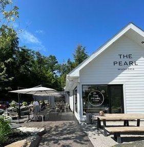 A white building with a picnic table and umbrellas in front of it.