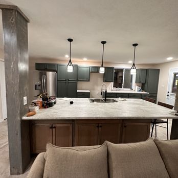 Modern kitchen with dark green cabinets, light countertops, and pendant lights.