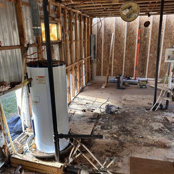 A gutted room with a water heater. Exposed wood framing, debris on the floor, and a bare wall.