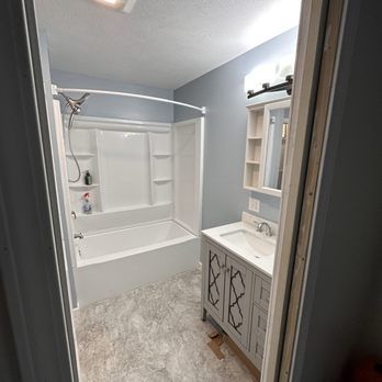 Bathroom with a white bathtub and vanity, light blue walls, and gray flooring.