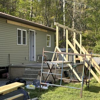 Green house with steps, wooden ramp under construction, scaffolding, and trees.
