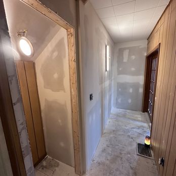 Hallway under construction with unfinished drywall, a door, and wood paneling.