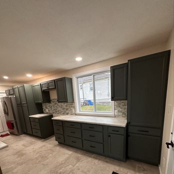 Dark green kitchen cabinets with white countertops, a window, and tile backsplash.