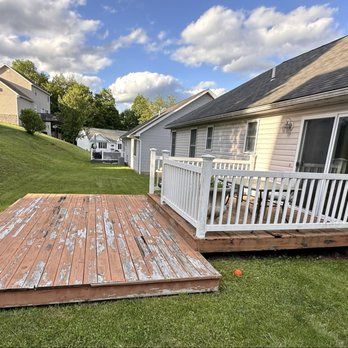 Backyard with two decks; one weathered, one with white railing. Houses and green grass under cloudy sky.