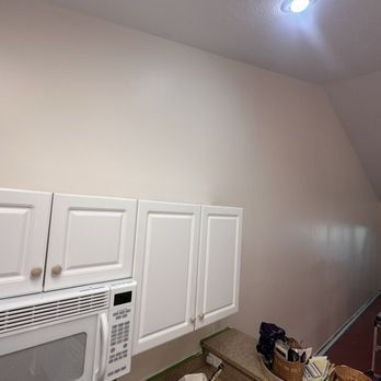 White kitchen cabinets under a cream-colored wall and angled ceiling, with a microwave.
