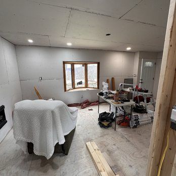 Room under construction; drywall, window, tools on table, armchair covered with a blanket.