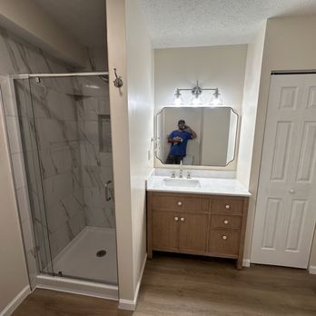 Bathroom with marble shower, vanity with mirror, and white door.