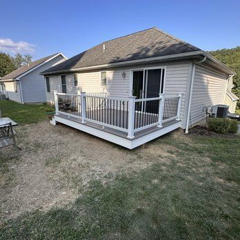 A small, gray deck with white railings and black spindles in front of a light-colored house.