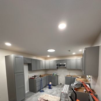 Kitchen under construction with gray cabinets and recessed lighting.