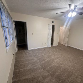 Empty room with carpet, three doors, a window with blinds, and a ceiling fan.