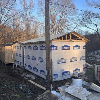 A partially constructed shed wrapped in Lowe's branded moisture barrier; a utility pole is in front.