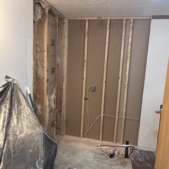 Interior wall under renovation, exposed studs, insulation, and electrical wiring.