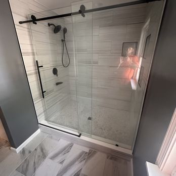 Modern glass shower with black fixtures and hardware. White marble-look tile walls and floor. Gray walls.