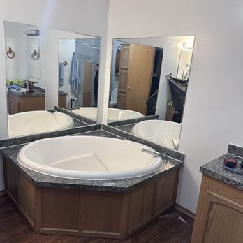 Bathroom with a corner jacuzzi tub, mirrors, and granite countertops. Brown cabinets.