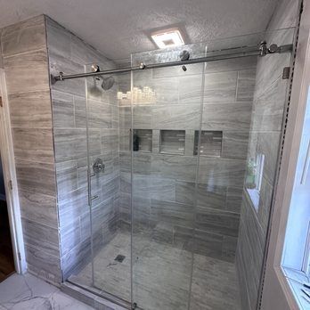 Modern shower with gray tiled walls, glass doors, and recessed shelves.