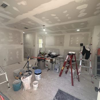 Room under construction, drywall installed, tools and materials scattered, unfinished ceiling with recessed lights.
