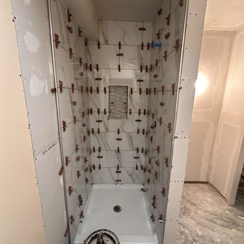 Shower stall in progress with white and marble-patterned tiles installed, tile spacers in place.