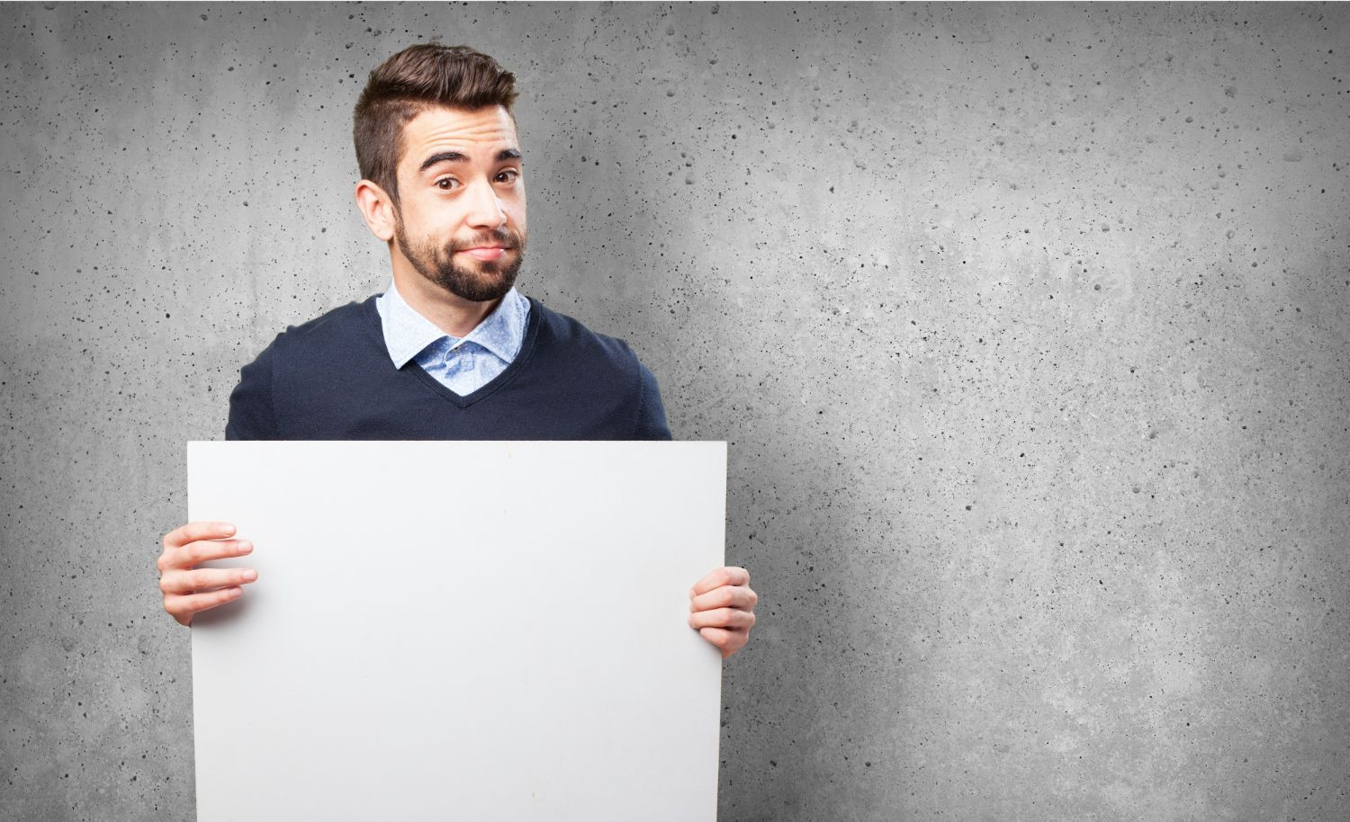 A man stands in front of a wall, holding a blank sign, ready to convey a message or idea