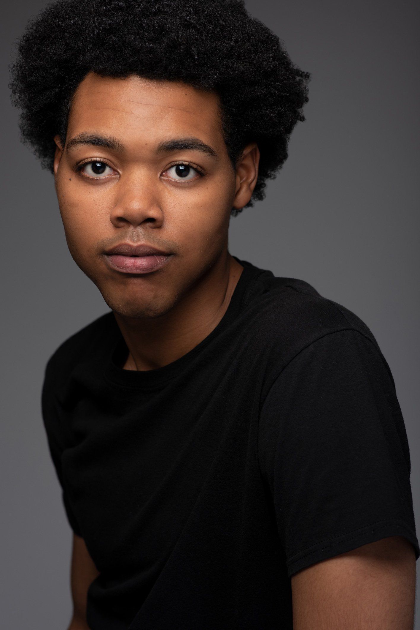 Portrait of a person in a black shirt against a gray background, looking at the camera.