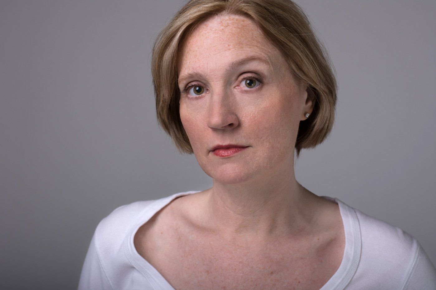 Portrait of a person with short blonde hair wearing a white top against a gray background