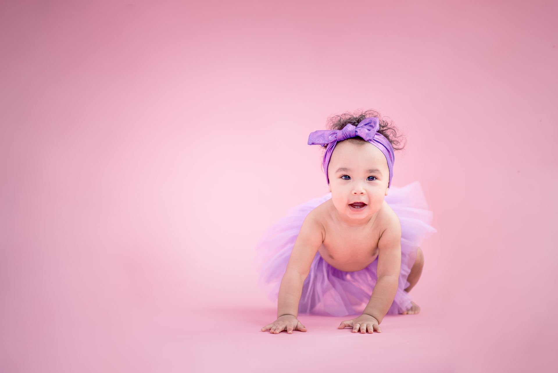 Baby in a purple tutu crawling on a pink studio backdrop