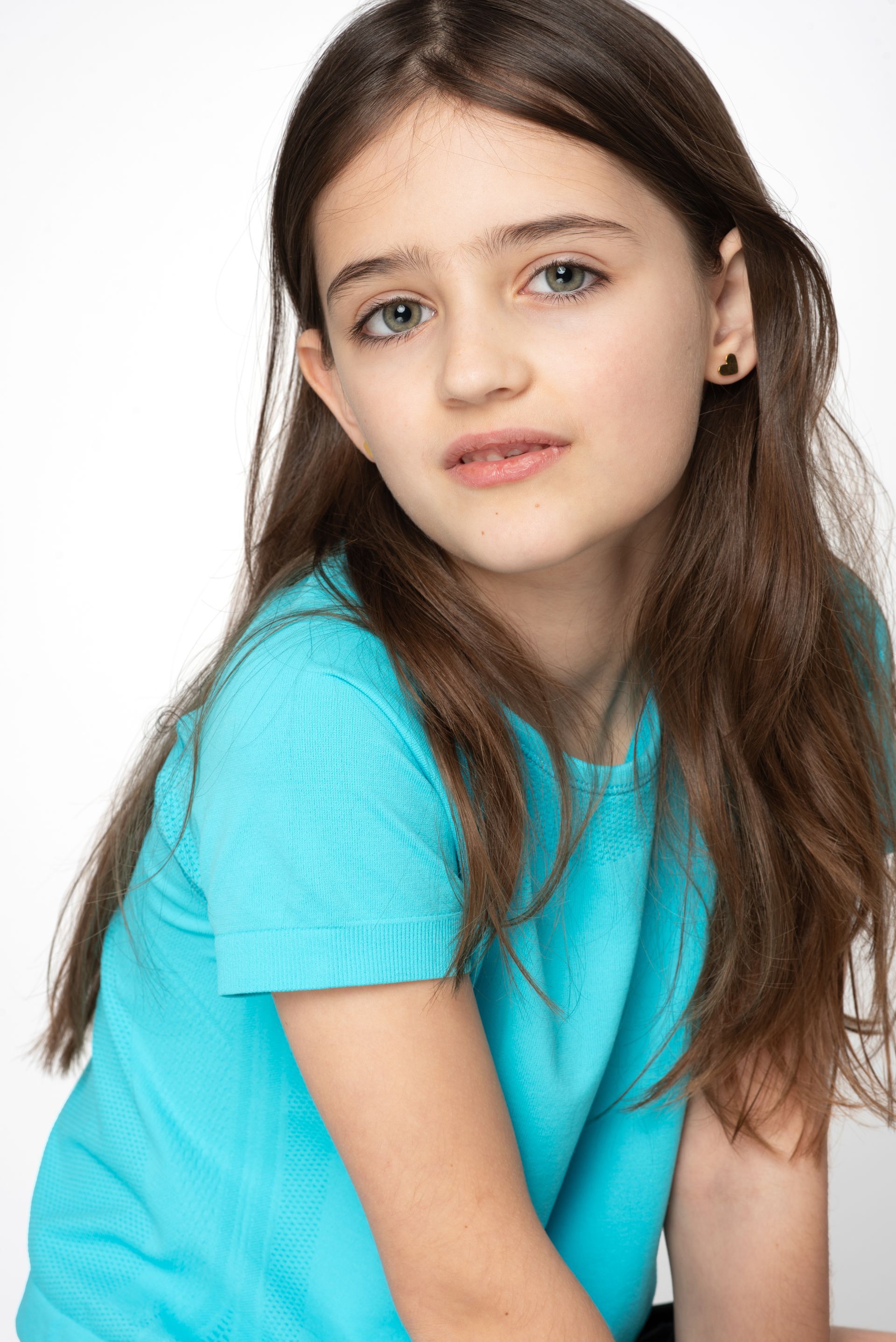 Portrait of a girl in a turquoise shirt, seated against a white background with a calm expression