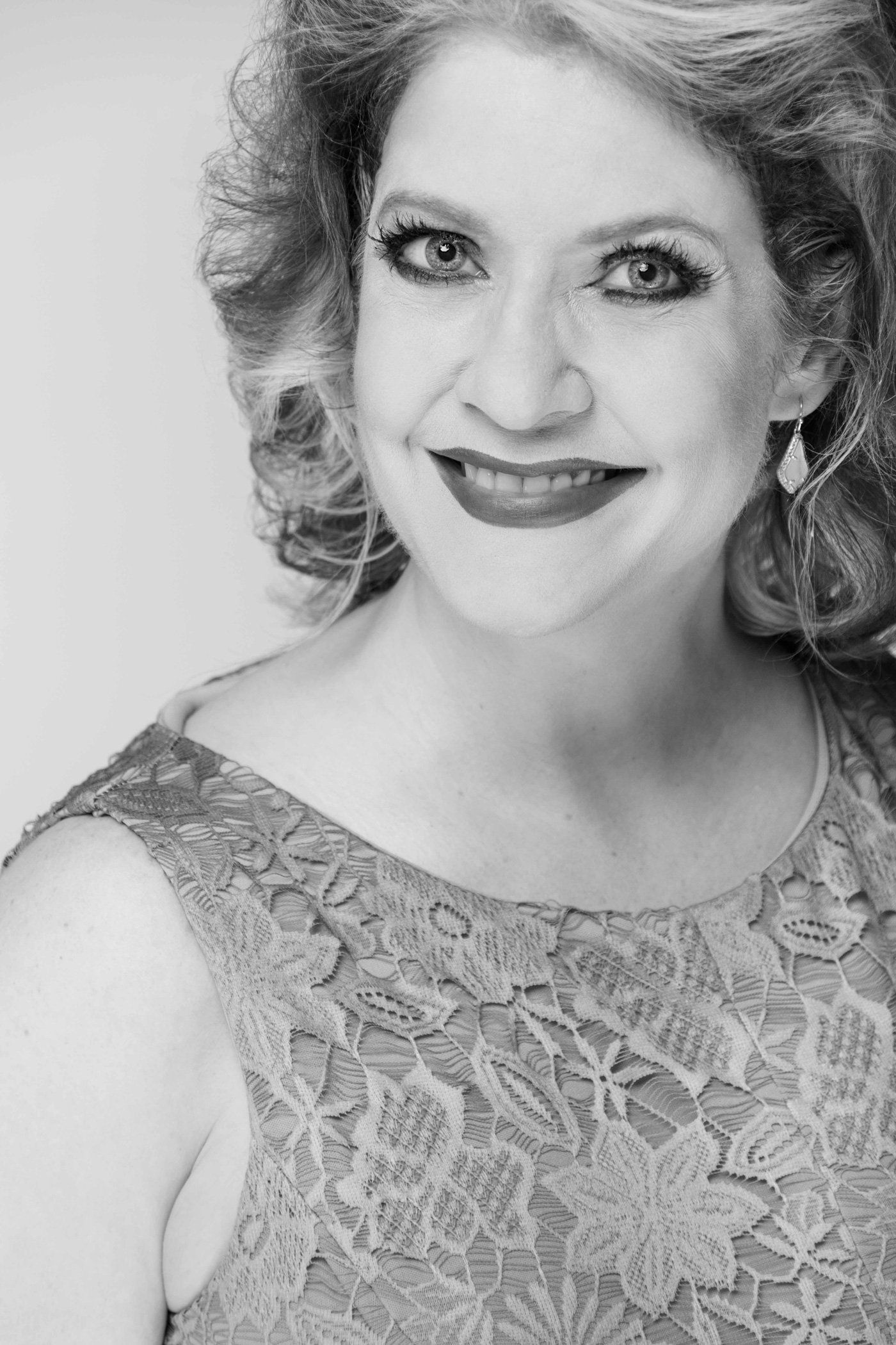 Smiling person in a lace dress, posed against a light background.