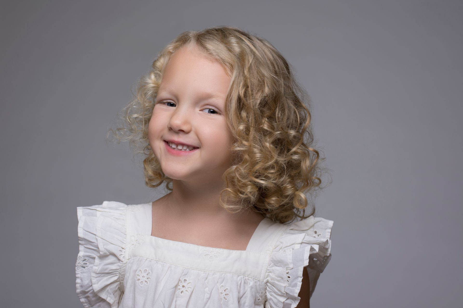 Smiling child in a white ruffled dress against a gray background