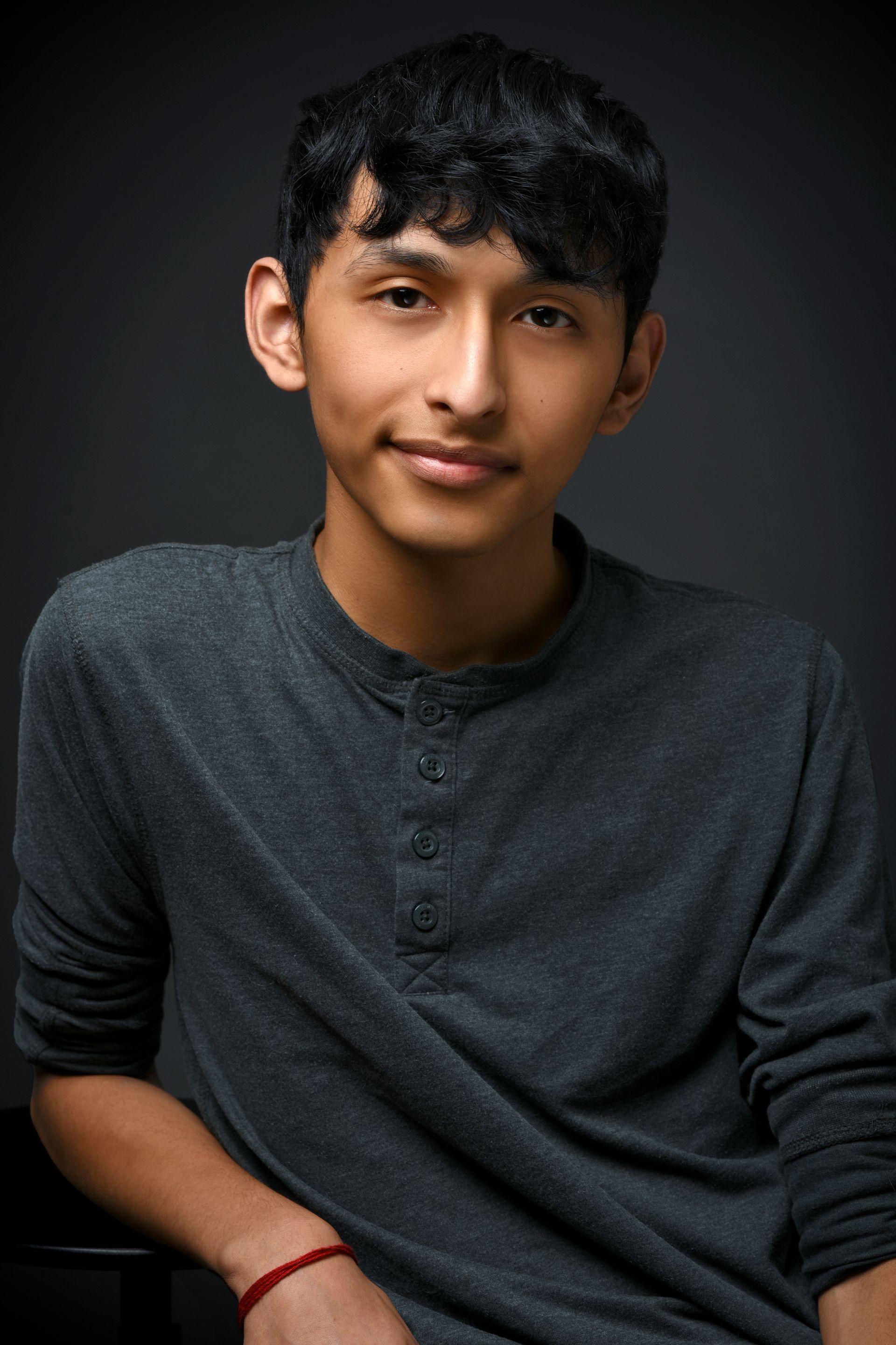 Person seated against a dark background, wearing a dark gray shirt and looking at the camera.