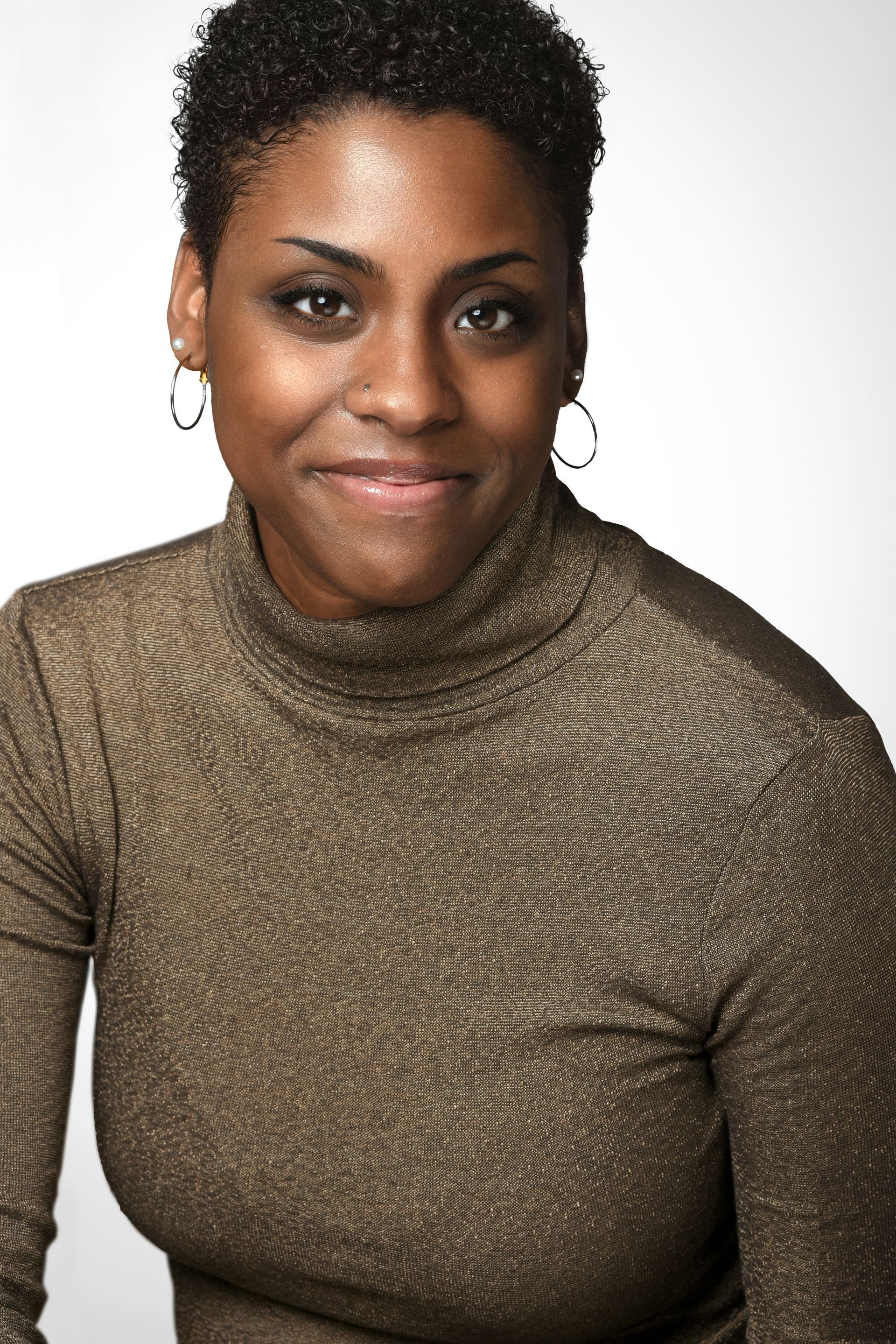 Smiling person in a brown turtleneck sweater against a light background