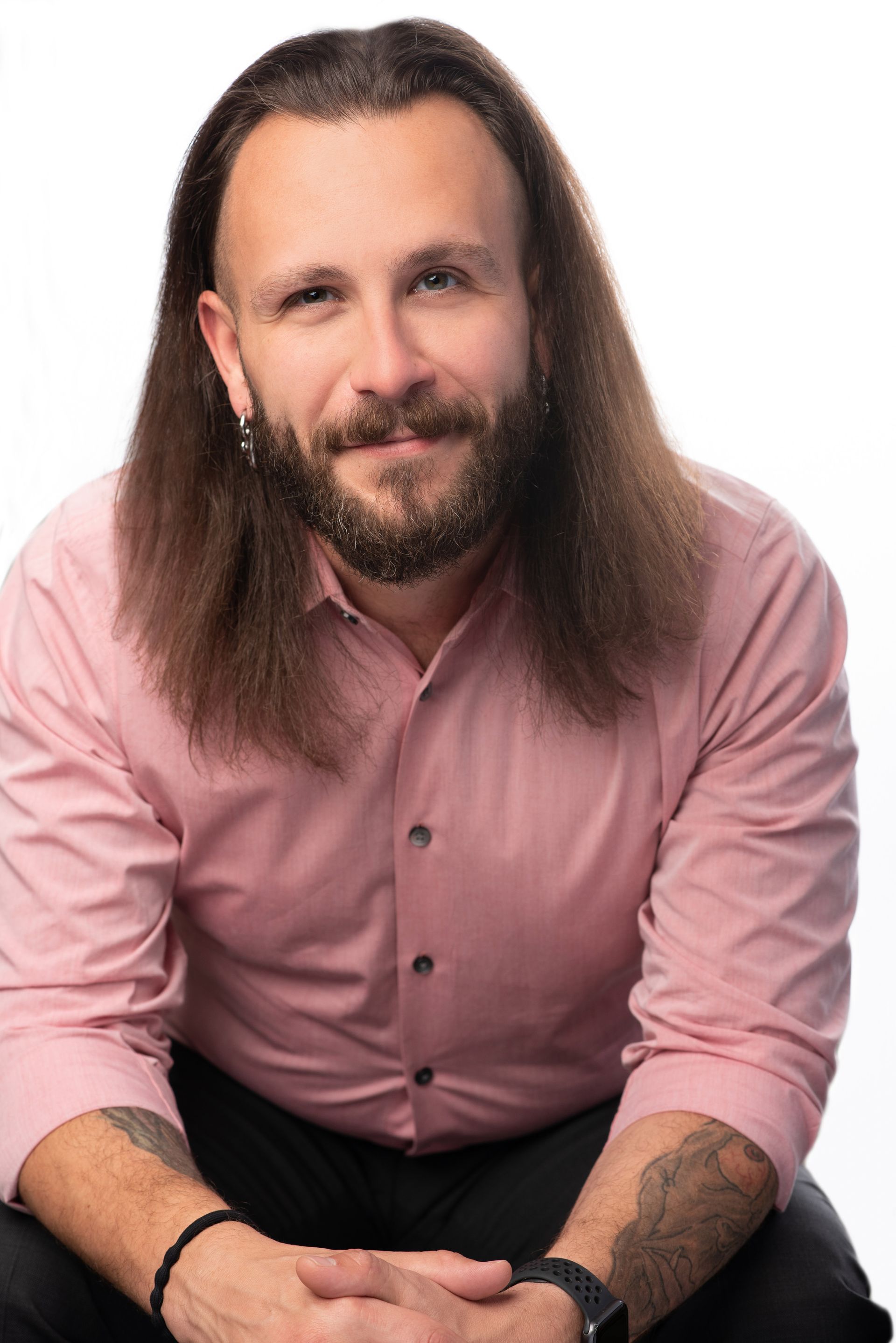 Smiling person in a pink shirt with long hair seated against a white background