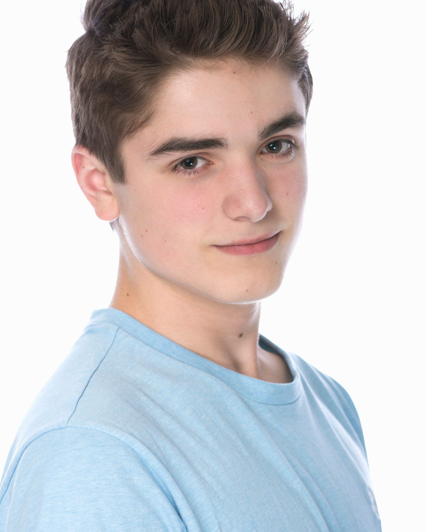 Young person in a light blue shirt, smiling slightly against a white background