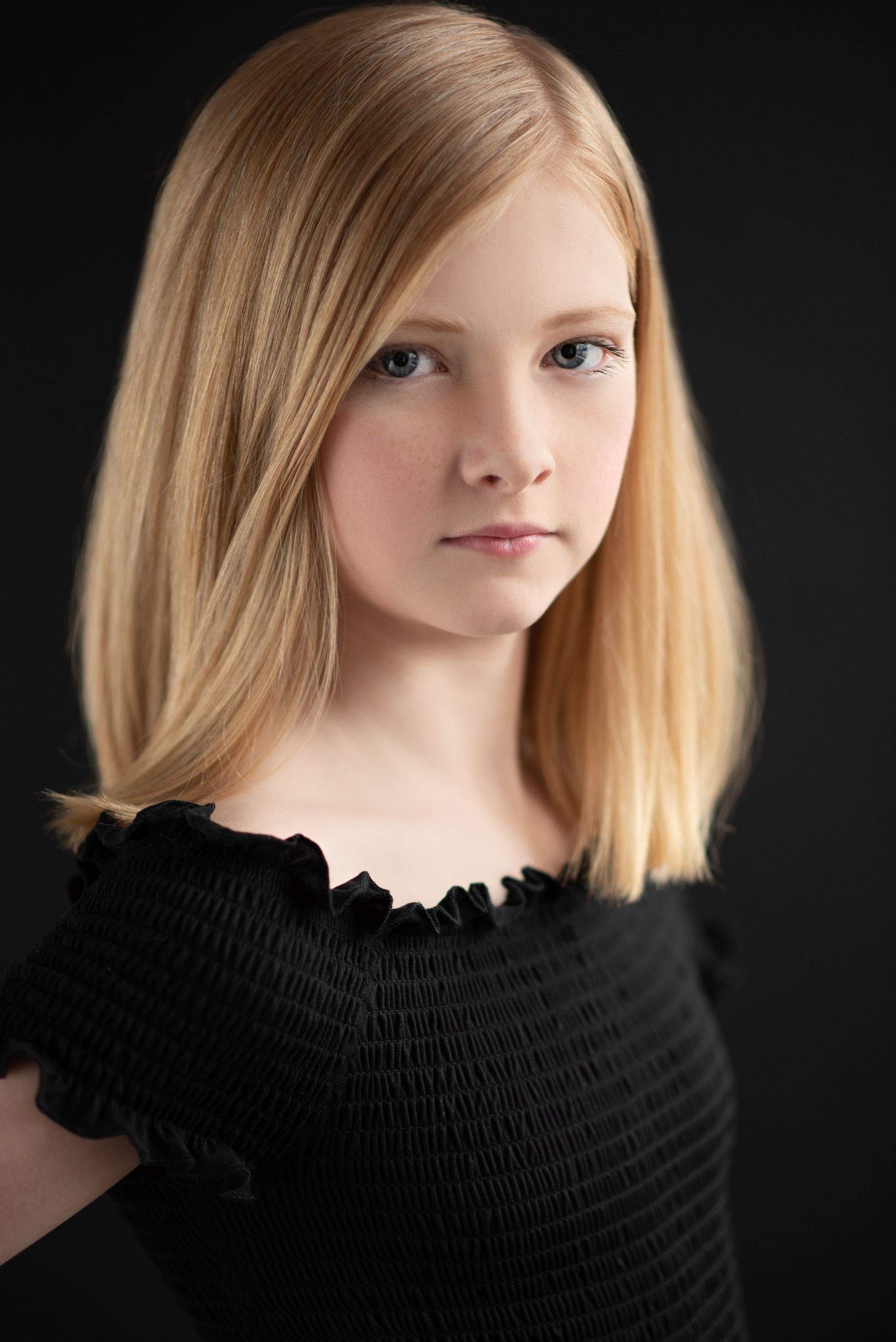 Portrait of a blonde person in a black top against a dark background