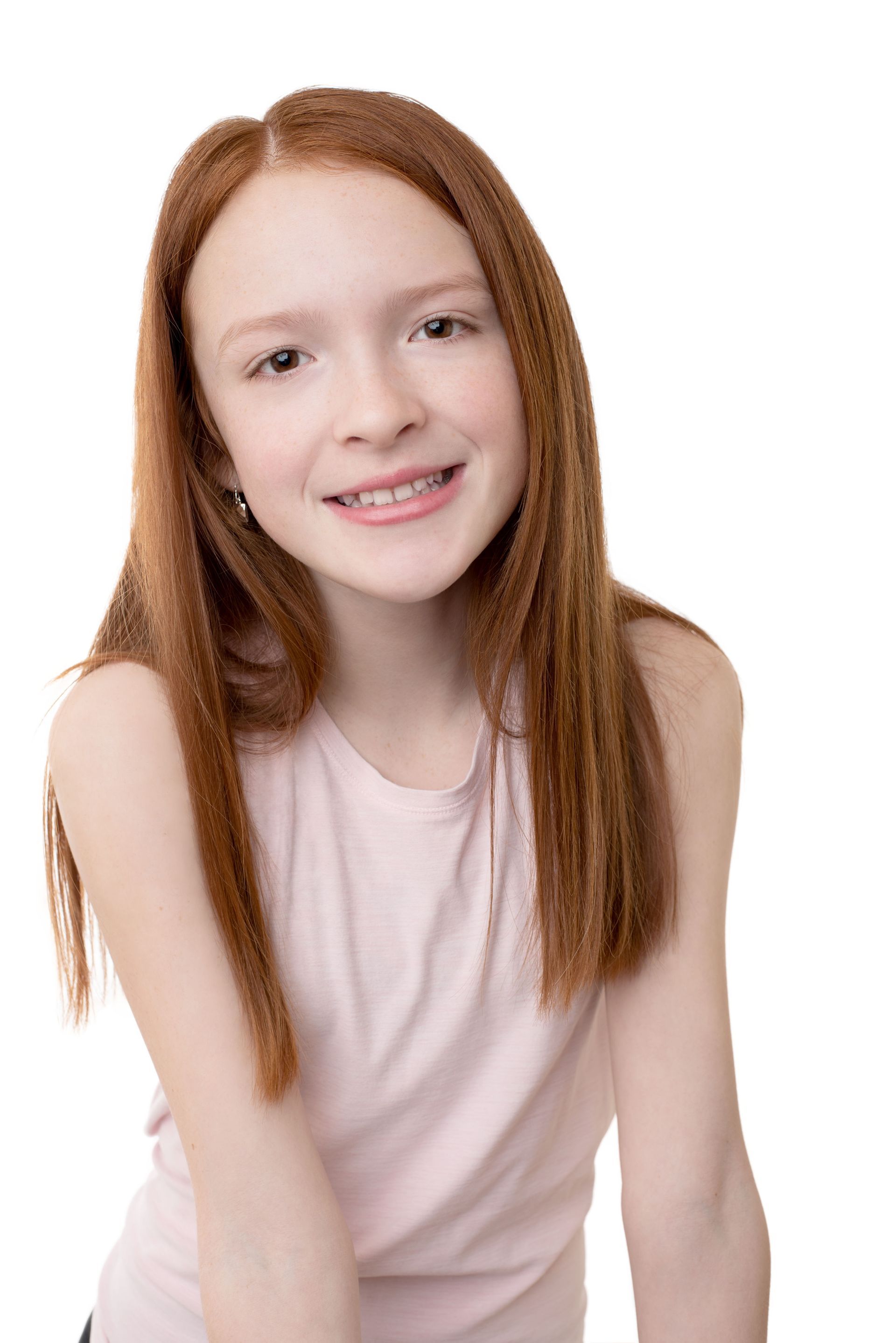 Smiling red-haired child in a pale pink sleeveless top against a white background