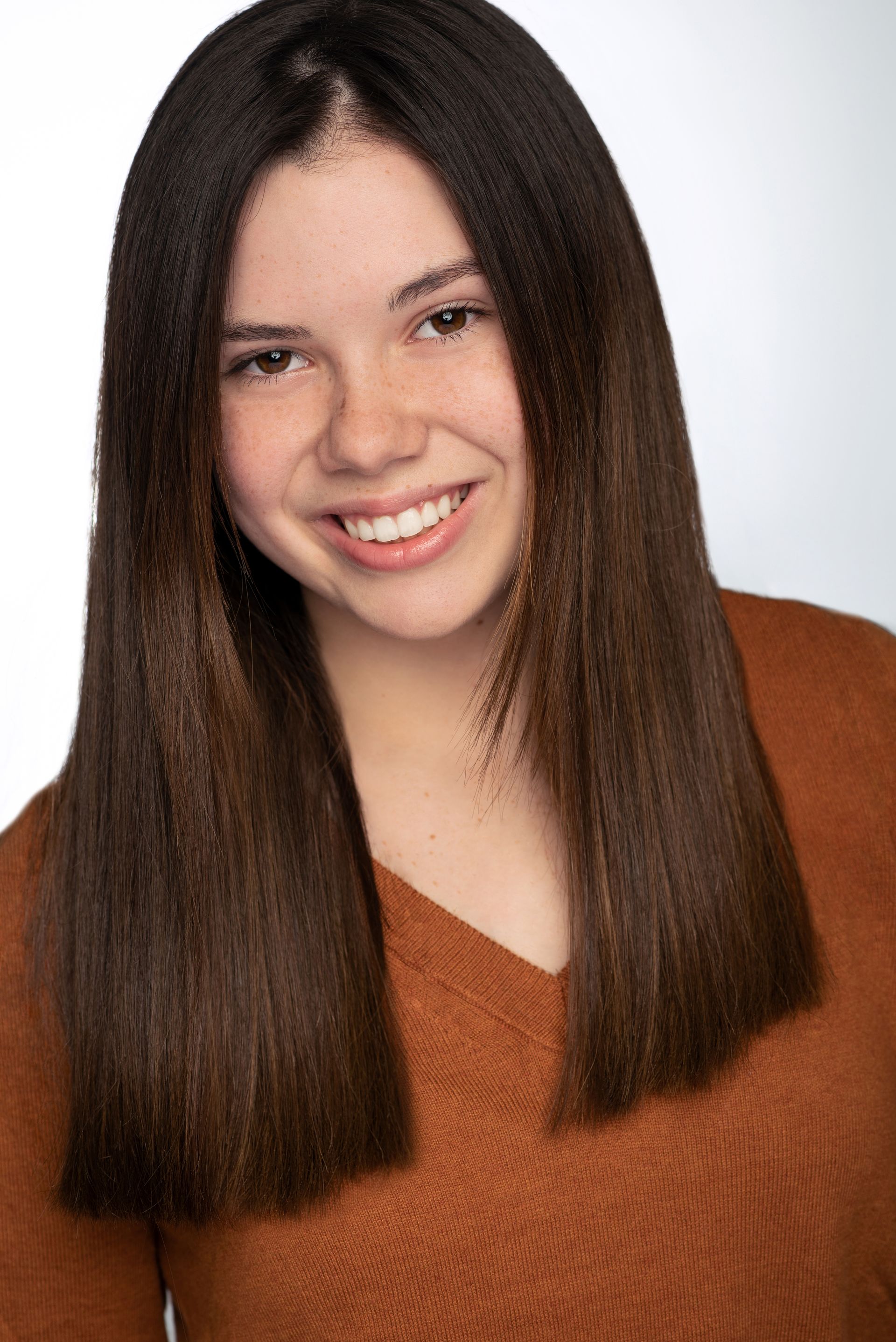 Smiling person with long straight brown hair wearing a rust-colored sweater against a white background