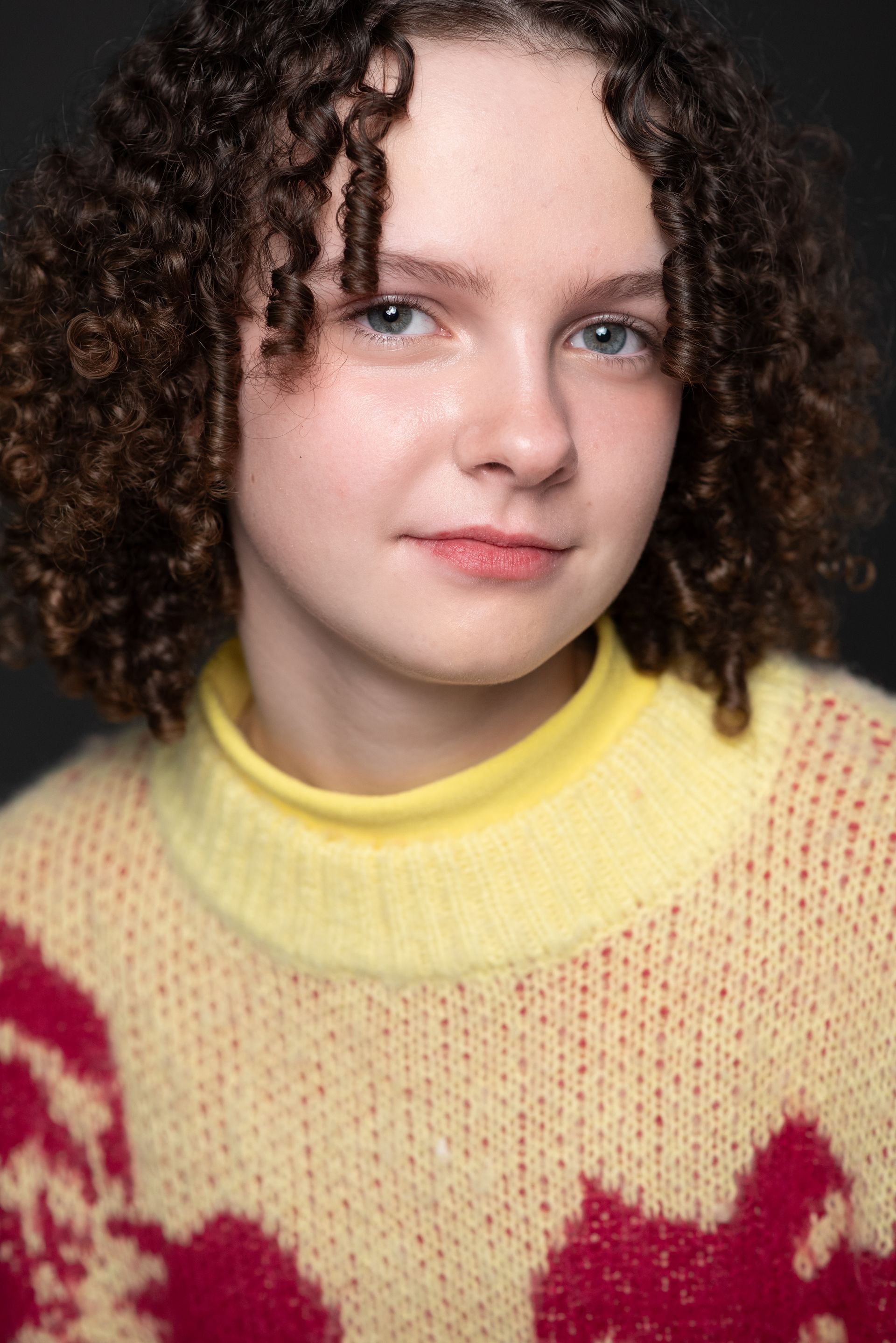 Portrait of a person with curly hair wearing a yellow sweater with red pattern, looking at the camera